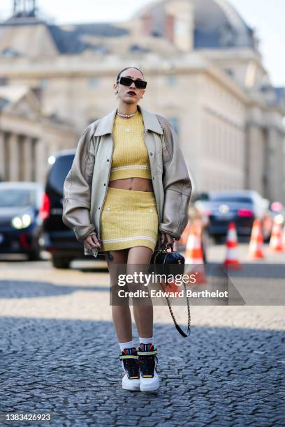 Hera Pradel wears black sunglasses, silver and pearls / logo pendant earrings from Chanel, a silver / rhinestones / pearls necklace from Chanel, a...