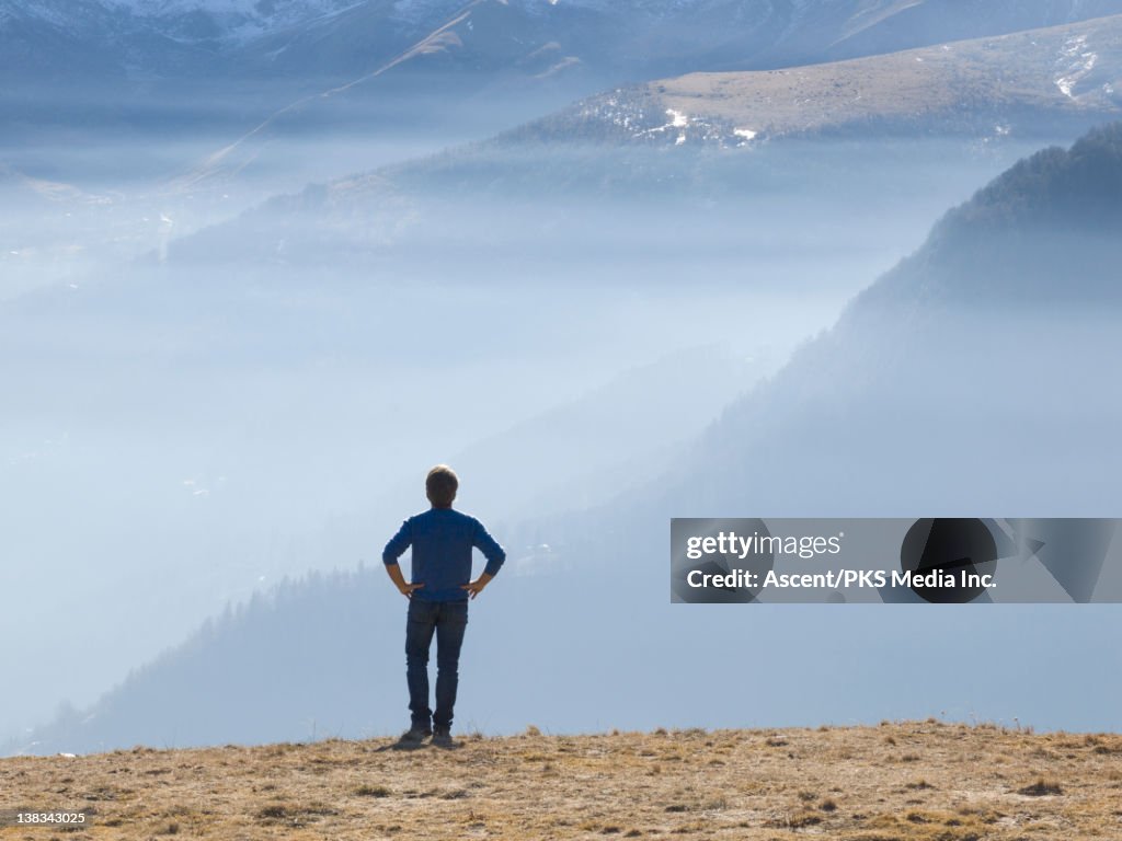 Man looks out over misty clouds/smog from meadow