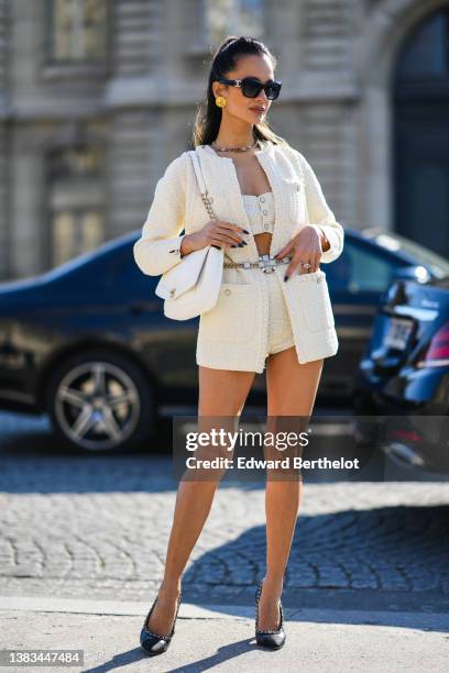 Anna Rosa Vitiello wears black sunglasses, gold earrings, a silver chain necklace from Chanel, a white wool buttoned shoulder-off / cropped top from...