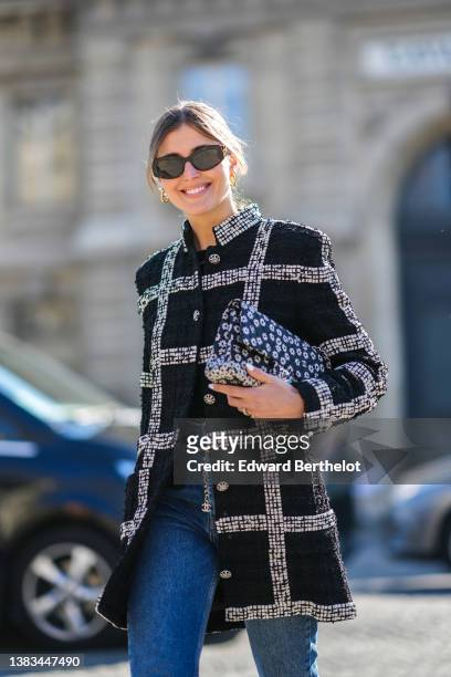 Darja Barannik wears black sunglasses, a black tweed with large white checkered print pattern buttoned coat from Chanel, a black with white flower...