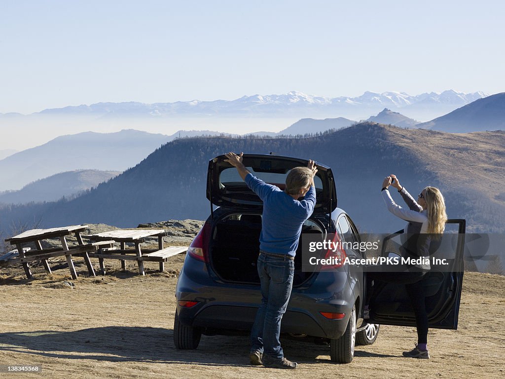 Couple at mtn picnic area with car, taking picture
