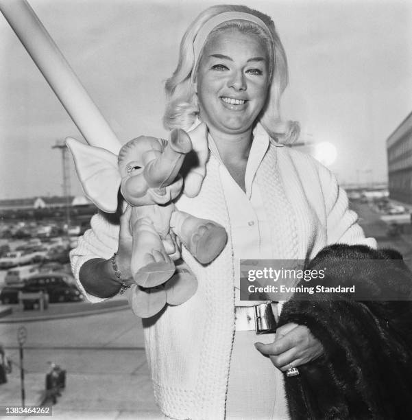 English actress Diana Dors at London Airport with a toy elephant, UK, 7th June 1963.