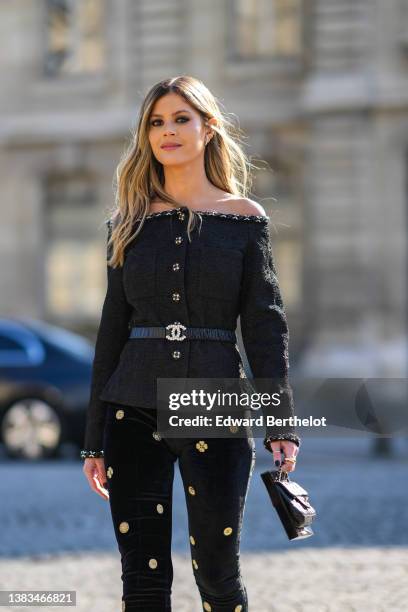 Lala Rudge wears a black tweed shoulder-off / buttoned jacket from Chanel, a black shiny leather with rhinestones logo buckle belt from Chanel, a...