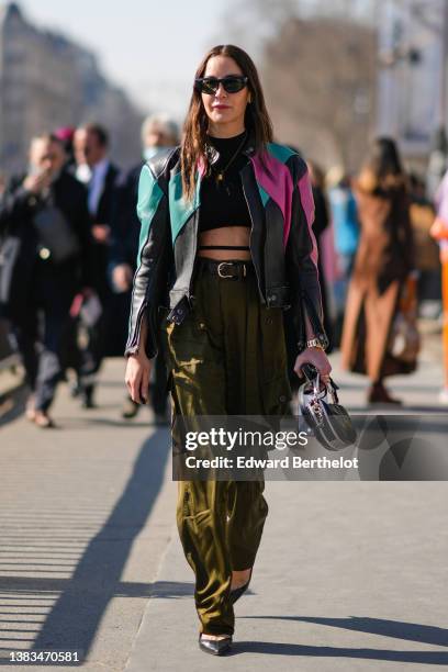 Ece Sukan wears black sunglasses, a black cropped top with laces waist, a black shiny leather with green and pink yoke zipper biker jacket, a black...