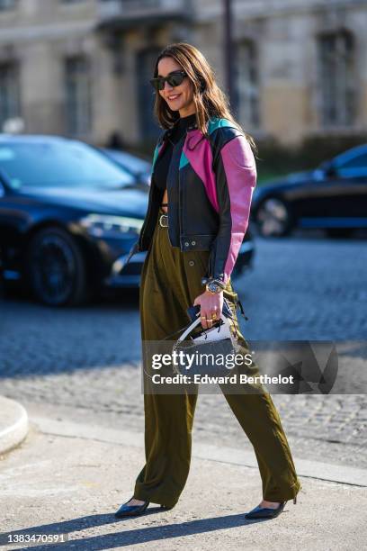 Ece Sukan wears black sunglasses, a black cropped top with laces waist, a black shiny leather with green and pink yoke zipper biker jacket, a black...