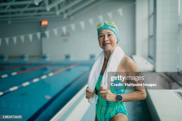 senior woman swimmer preparing for swim indoors in public swimming pool, looking at camera. - schwimmen schwimmbad stock-fotos und bilder