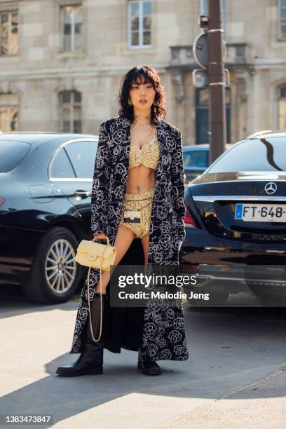 Influencer Xiayan Guo wears a black Chanel print coat, yellow matching tweed bra top and shorts, small Chanel belt purse accessory, yellow quilted...