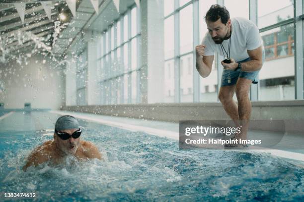 personal coach encouraging senior swimmer when swimming indoors in swimming pool. - swimming coach stock pictures, royalty-free photos & images