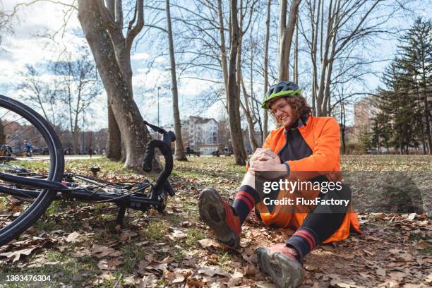 young man, sitting on the grass and holding his knee, after he injured himsefl during the cycling - adult riding bike through park stock pictures, royalty-free photos & images