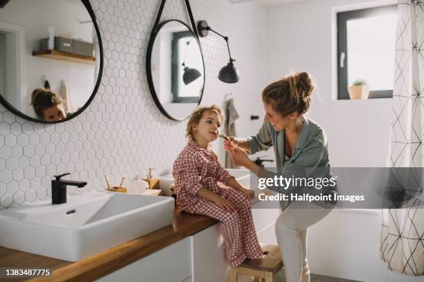 mother with small daughter indoors in bathroom in the morning at home, making plaits - women haircare stock-fotos und bilder