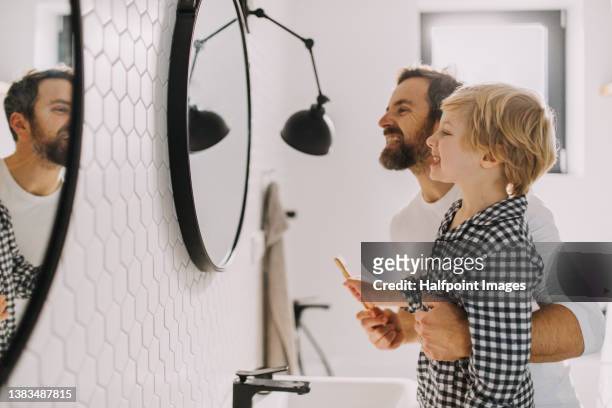 father with small child indoors in bathroom in the morning at home, brushing teeth. - routine stock-fotos und bilder