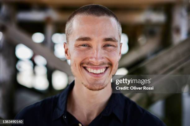 portrait of happy young man at wooden structure - shorthair stock-fotos und bilder