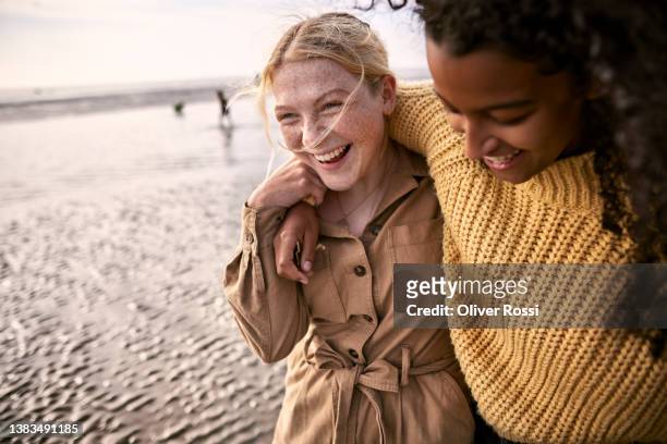 two happy female friends embracing on the beach - young adult stock-fotos und bilder