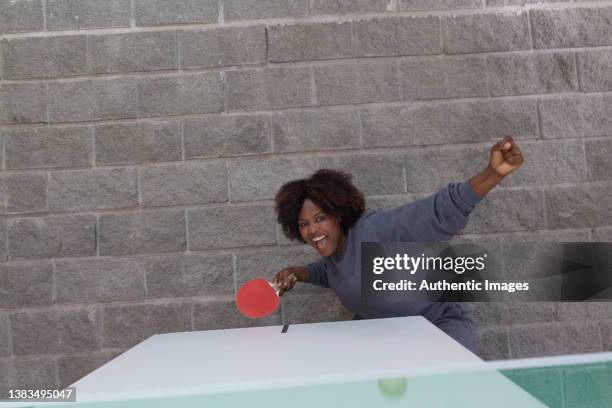 female african american business executive hitting ball while cheerfully playing  table tennis at leisure room - women's table tennis stockfoto's en -beelden