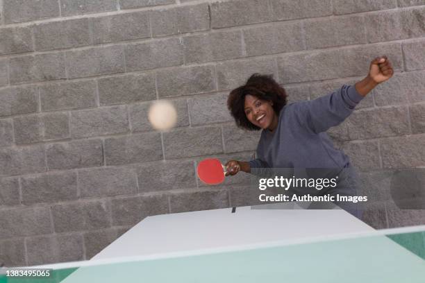 donna afroamericana business executive che colpisce la palla mentre gioca allegramente a ping pong nella sala ricreativa - black ping pong table foto e immagini stock