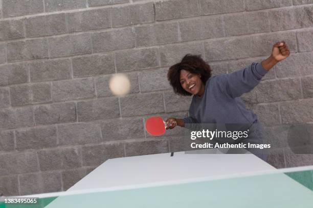 female african american business executive hitting ball while cheerfully playing  table tennis at leisure room - women's table tennis stockfoto's en -beelden