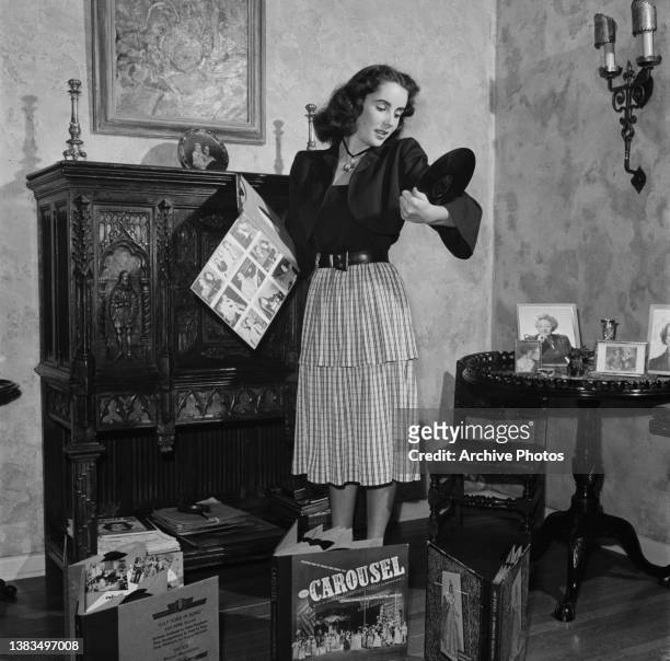 Actress Elizabeth Taylor listens to records, including the 1945 Broadway cast album of 'Carousel', USA, circa 1950.