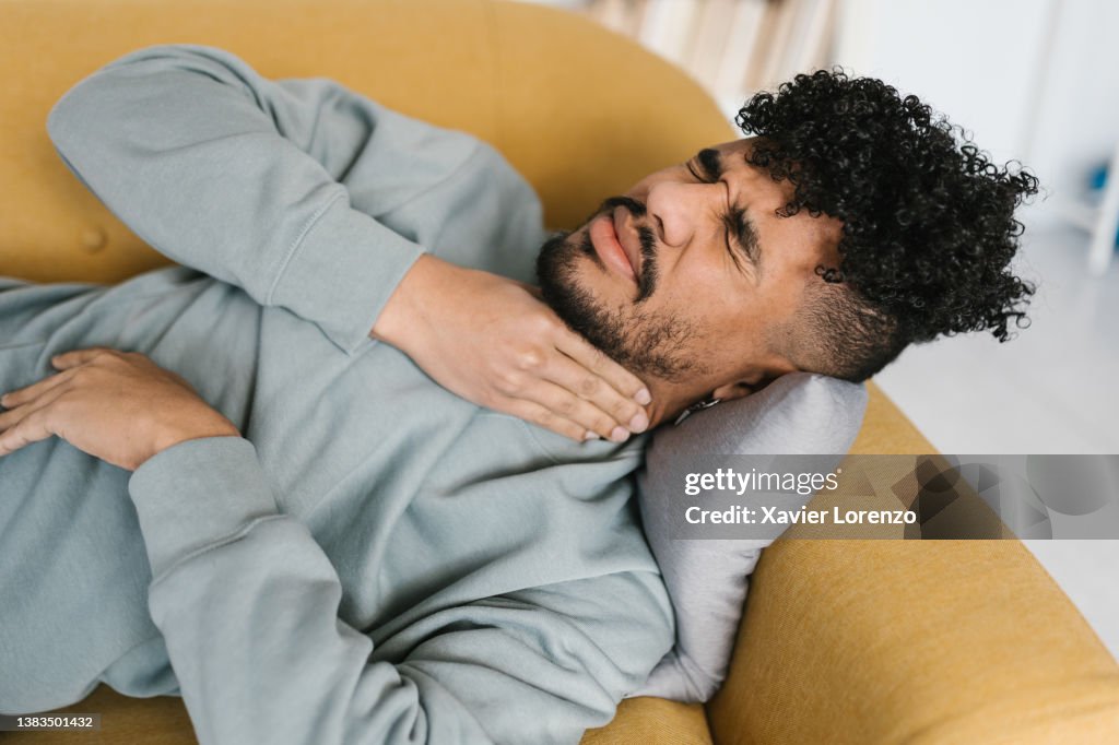 Young man with throat pain relaxing on sofa at home