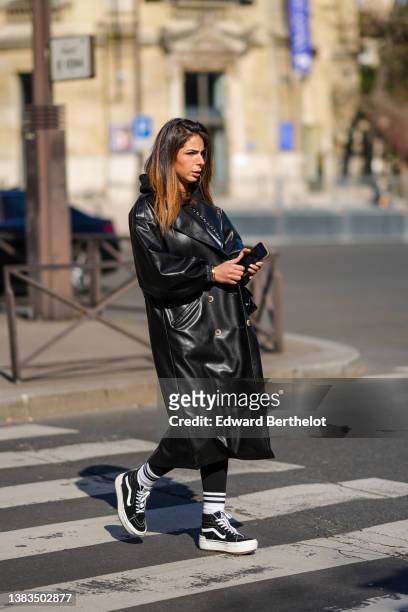 Guest wears a black hoodie sweater, a black shiny leather long coat, a black shiny leather crossbody bag from Chanel, a gold Love bracelet from...
