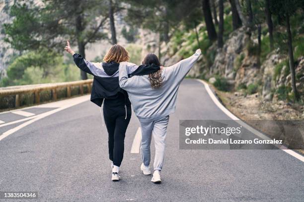 carefree women walking on asphalt road with raised arms - chándal fotografías e imágenes de stock