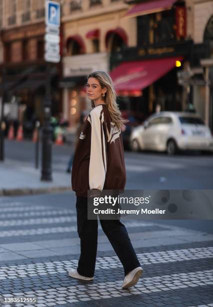 Millane Friesen wearing a brown college jacket, white top, black pants, white nike air force one sneaker and gold jewelry on March 07, 2022 in Paris,...