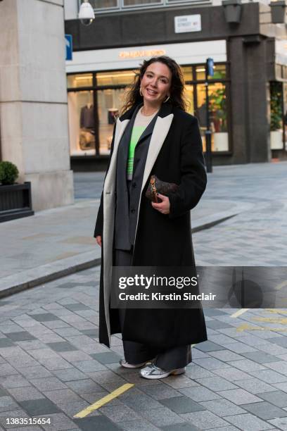 Naomi May wears a Harris Tapper coat, Louis Vuitton bag, Asics trainers, grey suit and a green and white jumper during London Fashion Week February...