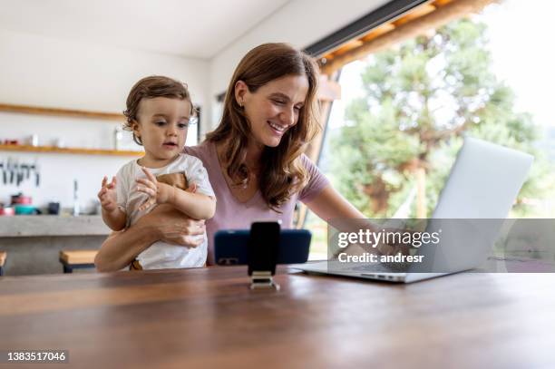 happy mother working on her laptop while her son watches tv on her cell phone - balancing act cartoon stock pictures, royalty-free photos & images