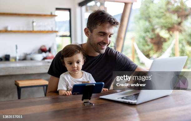 happy father working on his laptop while his son watches tv on his cell phone - work video call stock pictures, royalty-free photos & images