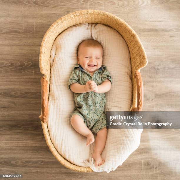 11-week-old baby boy wearing a green floral button down romper laying in a cozy gauzy cotton blanket in a wicker moses basket - gebloemd shirt stockfoto's en -beelden