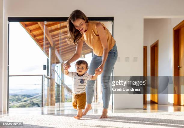 toddler learning how to walk at home with the help of his mother - walker stockfoto's en -beelden