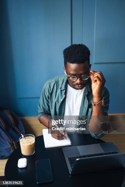 handsome male student using his laptop computer in a coffee shop - reading glasses on table stock pictures, royalty-free photos & images