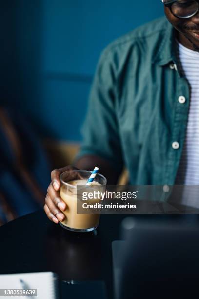 uno studente anonimo che beve caffè mentre usa il suo computer portatile in un bar - iced coffee foto e immagini stock