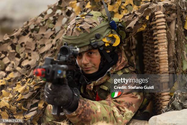 An Italian Army soldier holds an engagement position while camouflaged and under a camouflage tent during the Volpe Bianca Military Exercise on March...