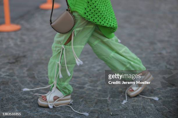 Olivia Neill wearing black shades, golden jewelry, a green knit pullover with cutouts, a brown Stella McCartney bag, green pants and white plateau...