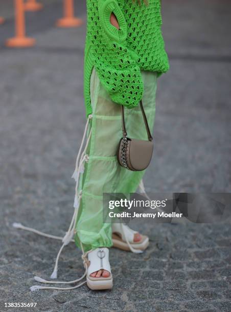 Olivia Neill wearing black shades, golden jewelry, a green knit pullover with cutouts, a brown Stella McCartney bag, green pants and white plateau...