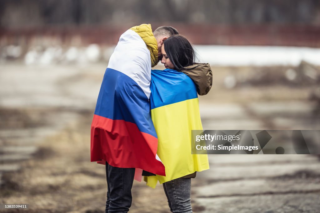 Symbol of peace between Russia and Ukraine as young couple hugs dressed in their national flags.