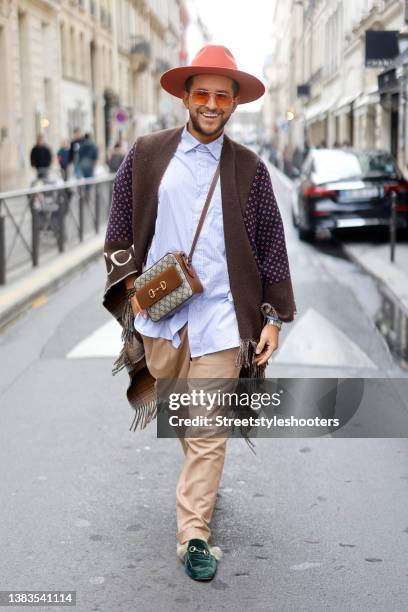 Influencer Luca Bazzanella wearing a red, beige, blue and brown wool logo GG poncho cape by Gucci, beige side buckle fastening trousers by Lardini, a...