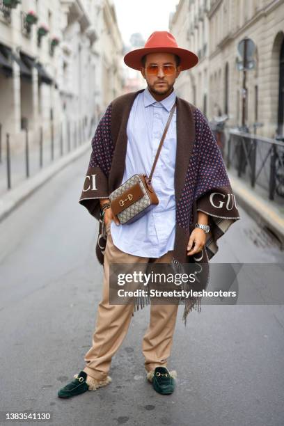 Influencer Luca Bazzanella wearing a red, beige, blue and brown wool logo GG poncho cape by Gucci, beige side buckle fastening trousers by Lardini, a...