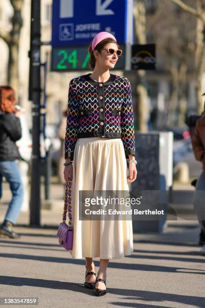 Guest wears a pink oversized headband, brown vintage sunglasses, a black tweed with multicolored wavy striped print pattern jacket from Chanel, a...