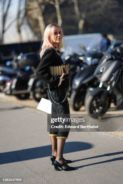 Guest wears a black shiny leather with gold pendant necklace from Chanel, silver rings, a black tweed jacket, a black and beige shiny leather striped...