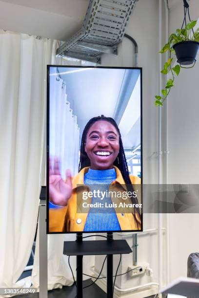african woman on video call waving hands to colleagues in office - vertical tv stock pictures, royalty-free photos & images