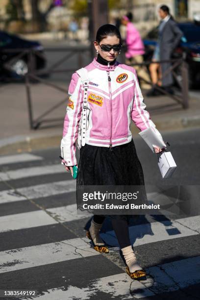 Guest wears black sunglasses, a black turtleneck pullover, a pale pink and white leather zipper biker jacket with red and yellow embroidered yoke...