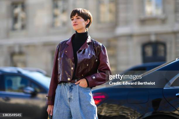 Guest wears a black turtleneck pullover, a burgundy shiny leather cropped biker jacket from Chanel, high waist blue faded denim large pants, a black...