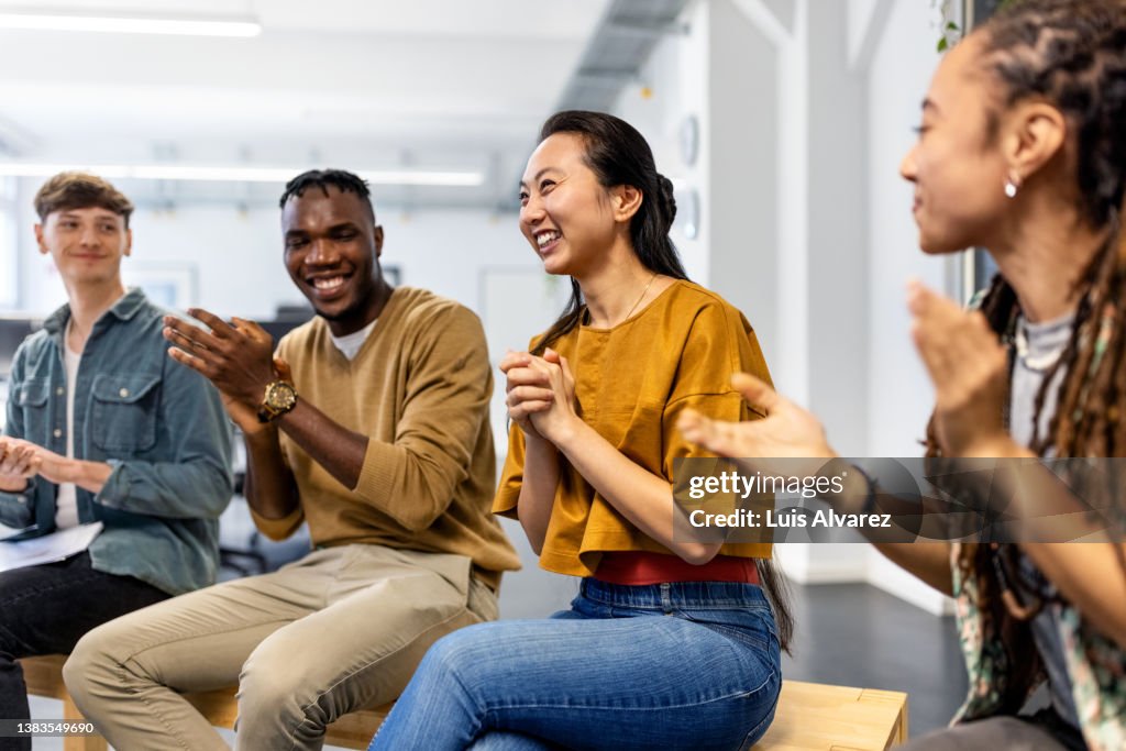 Group of business people sitting in a circle clapping hands in meeting