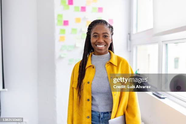 portrait of a positive young woman standing in office - holding laptop stock pictures, royalty-free photos & images