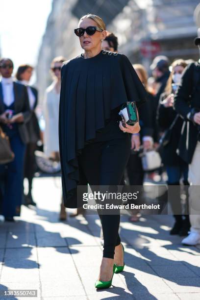 Guest wears black sunglasses from Louis Vuitton, a black pleated / accordion asymmetric cloak from Louis Vuitton, black legging pants, a black and...