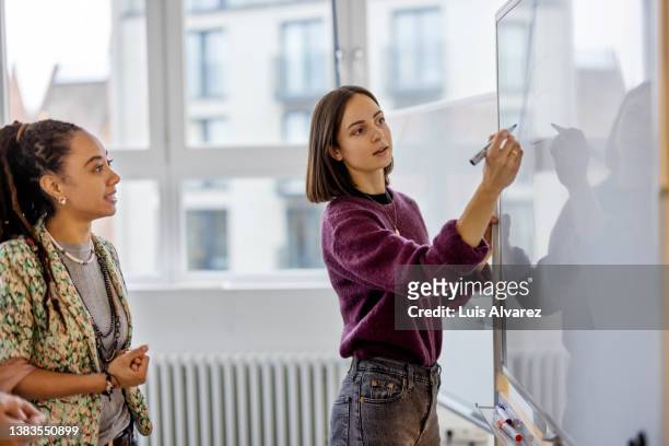 businesswoman brainstorming ideas on whiteboard with colleague - blazer viola foto e immagini stock