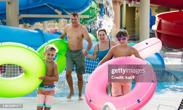 family at waterpark carry inflatable rings to lazy river - inflatable playground stock pictures, royalty-free photos & images