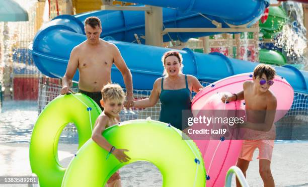 family at waterpark carry inflatable rings to lazy river - lazy river stock pictures, royalty-free photos & images