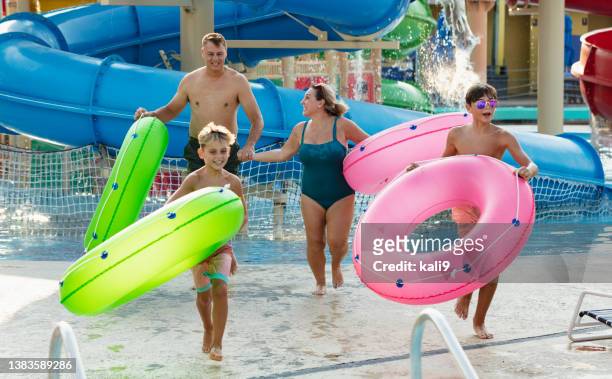 family at waterpark carry inflatable rings to lazy river - lazy river stock pictures, royalty-free photos & images